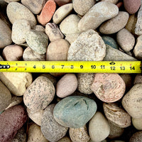 Close-up of Western Mountain Cobble Stone 2–4 inch showing and measuring tape with vibrant blue, white, pink, green, tan, gray, and black color variation