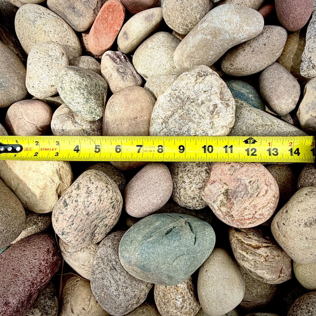 Close-up of Western Mountain Cobble Stone 2–4 inch showing and measuring tape with vibrant blue, white, pink, green, tan, gray, and black color variation